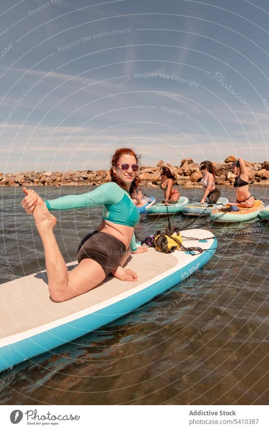 Cheerful women in one leg pigeon yoga pose over paddleboard trainer practice exercise stretch balance wellness fitness sup sport sea ocean group together