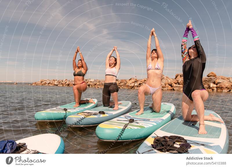 Group of women doing yoga in warrior 1 pose beach stretch practice balance warrior pose exercise activity coast kneel position wellbeing female ocean wellness