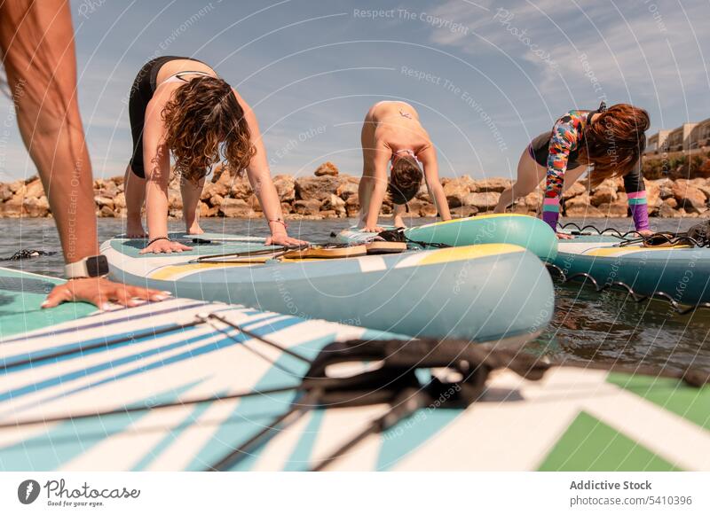 Women practicing yoga in forward fold pose on paddleboard practice exercise high plank fitness sea wellbeing summer women group arms raised training sky