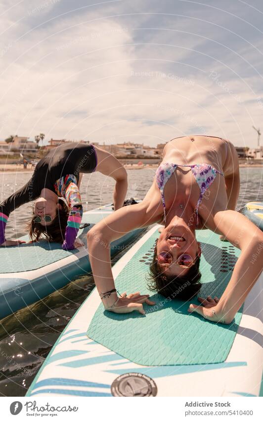 Women doing yoga on paddleboard in daylight women girlfriend practice half wheel flexible balance swimwear seawater young female cloudy blue sky summer