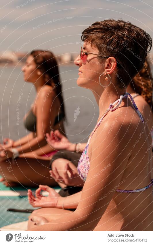 Young women sitting in Padmasana pose on paddleboards yoga lotus meditate practice calm mudra swimwear concentrate young female summer recreation zen vacation