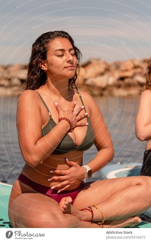 Calm female in swimwear breathing during SUP yoga woman sup yoga paddleboard sup board meditate balance zen seaside practice calm harmony pose wellness relax