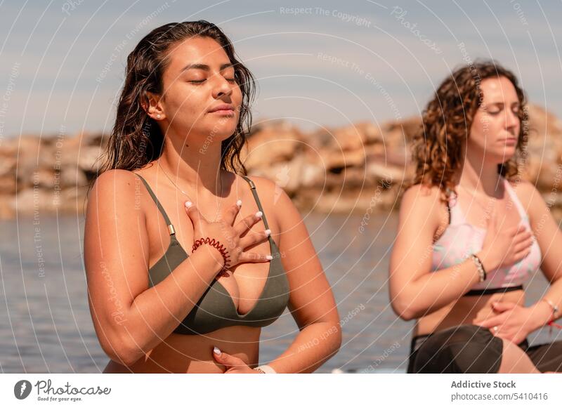 Women practicing meditation during SUP yoga on seaside women sup yoga paddleboard sup board meditate balance zen breath female practice calm harmony pose