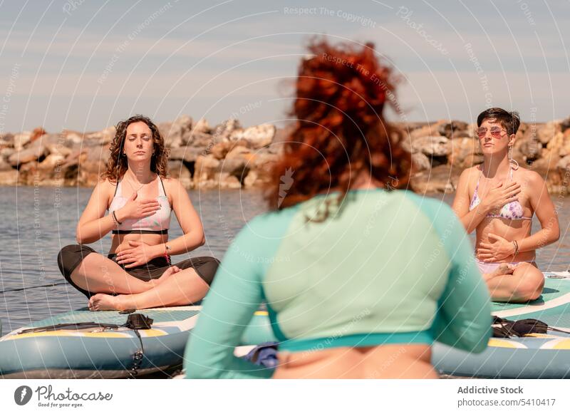 Women practicing meditation during SUP yoga on seaside women sup yoga paddleboard sup board meditate balance zen breath female practice calm harmony lady pose