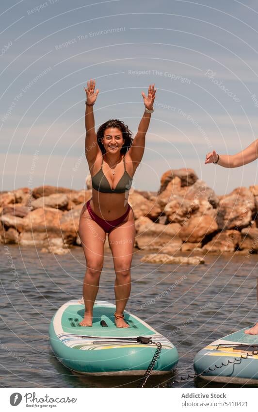 Cheerful woman with raised arms warrior 1 yoga pose on paddleboard exercise practice fitness sea balance warrior pose shield happy wellbeing virabhadrasana