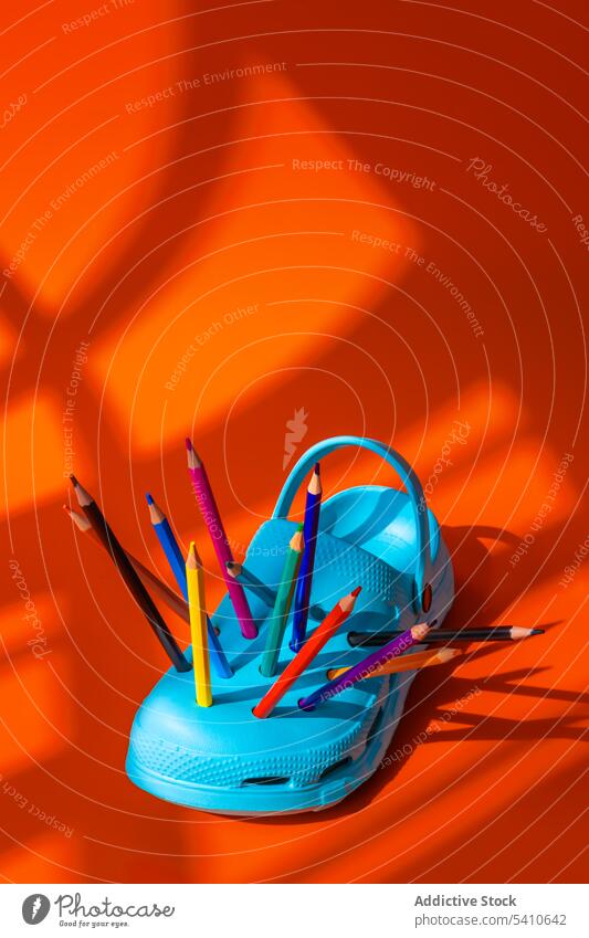 Multicolored pencils into the holes of blue clogs shoe colorful creative plastic footwear art bright equipment orange vivid vibrant multicolored material