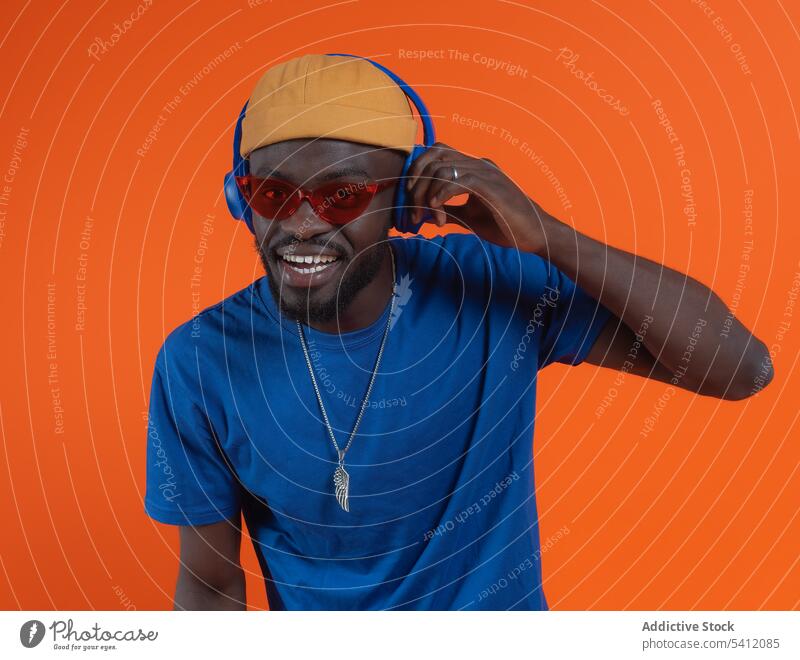 Stylish black man with headset and sunglasses cheerful happy smile style casual outfit hat portrait optimist glad joy young studio shot cool glee expressive