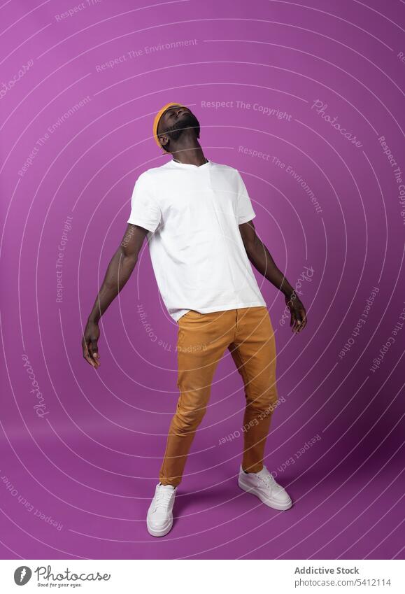 Black young man in cap standing with eyes closed in purple wall room posture tilt head backbend pink male ethnic african american black casual dress style guy