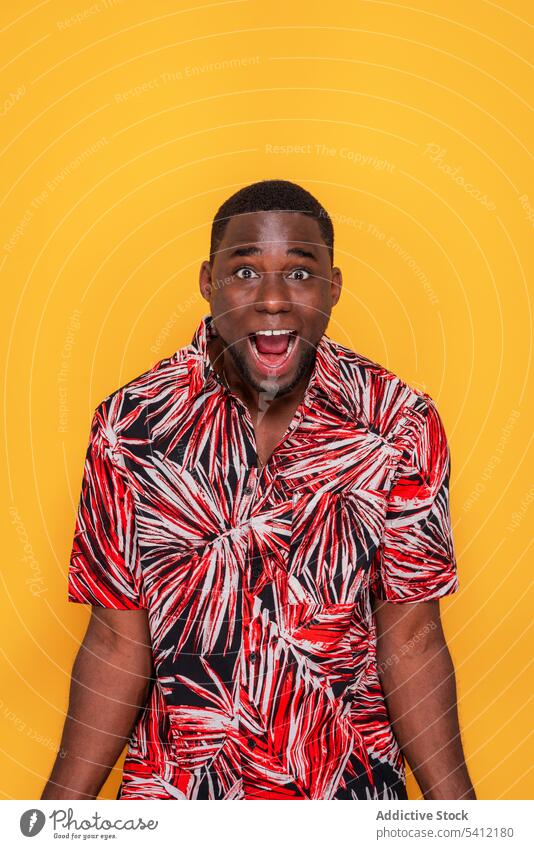 Surprised young black man standing against yellow background trendy surprise amazed style outfit gesture fashion apparel astonish mouth opened positive