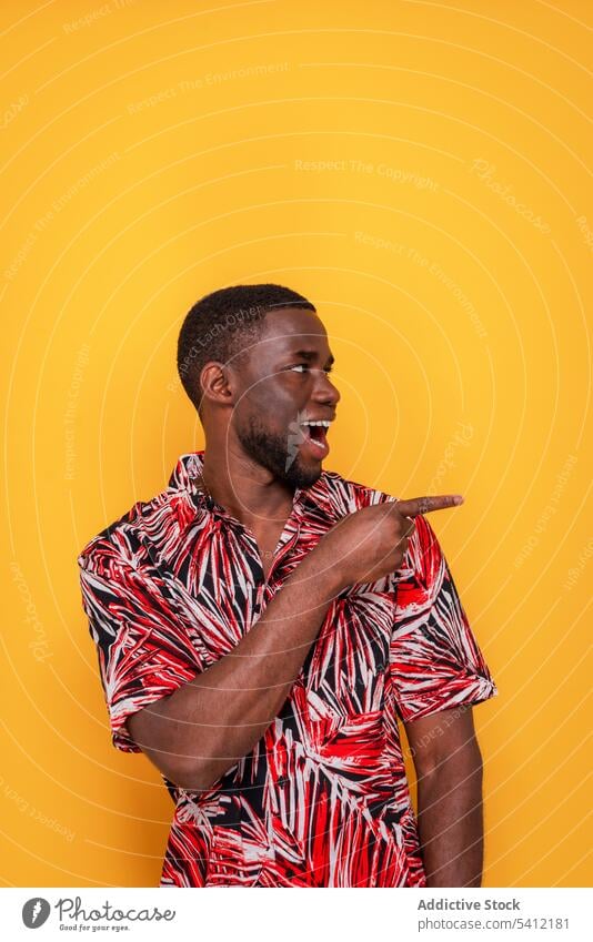 Cheerful black man pointing finger while looking away trendy style confident fashion colorful portrait cheerful bright studio shot modern beard vivid