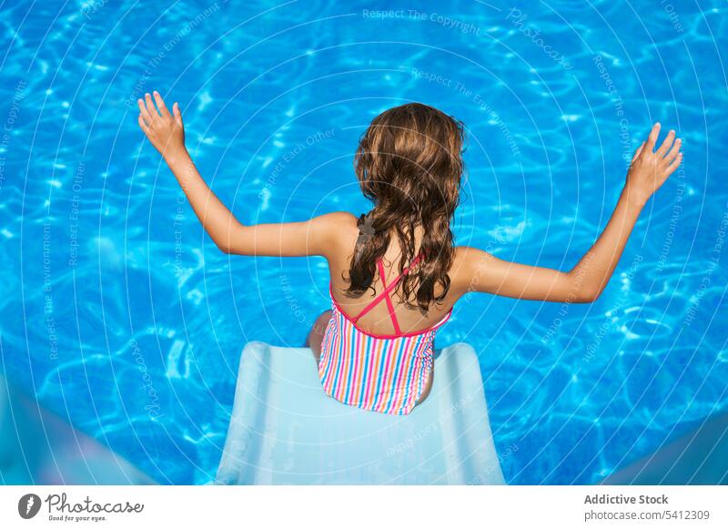 Back view of girl with raised hands by tip of slide in swimming pool vacation summer water resort swimwear sea holiday enjoy kid summertime rest swimsuit