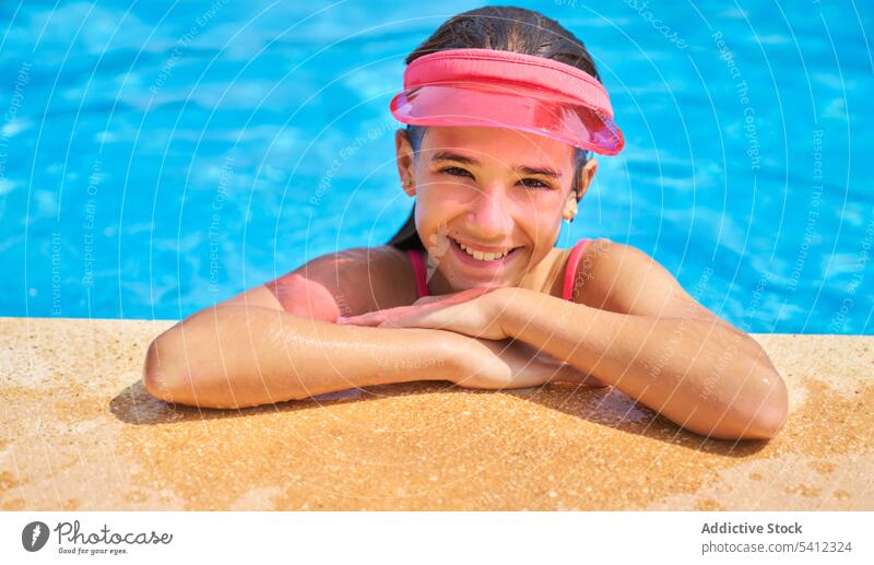 Young girl with sun visor cap relaxing with hands on poolside portrait smile happy enjoy rest vacation water kid child holiday cute resort adorable cheerful