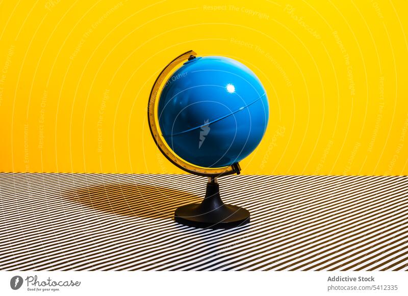 Globe placed on striped surface globe unfinished stationery bright colorful earth geography blue world sphere continent yellow table simple minimal element