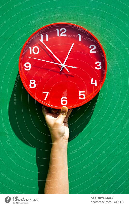 Crop hand holding red clock in green studio person time circle hour minute show round wall deadline bright concept creative shape punctual demonstrate material