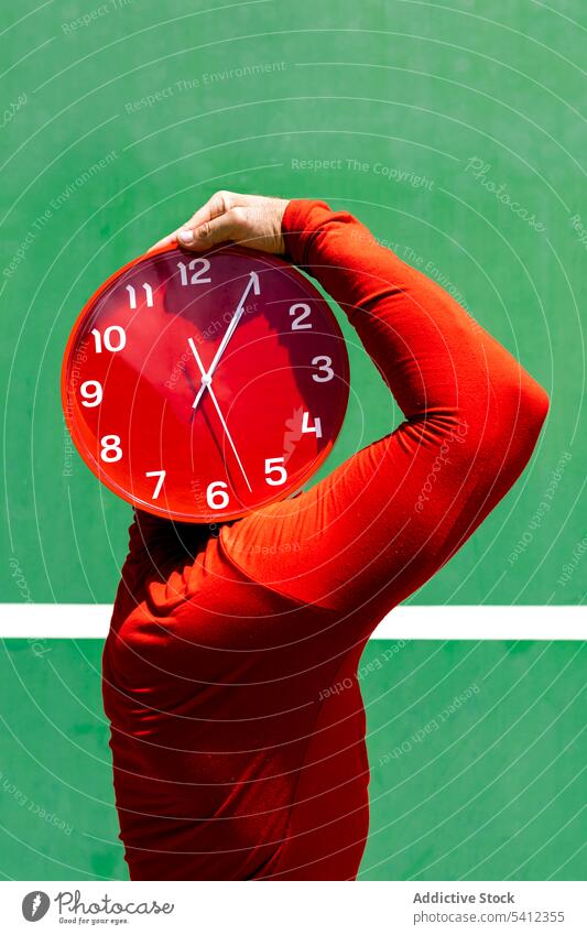 Anonymous person covering face with red clock time hide cover face hour hurry punctual concept mystery minute circle bright round deadline outfit vivid stress