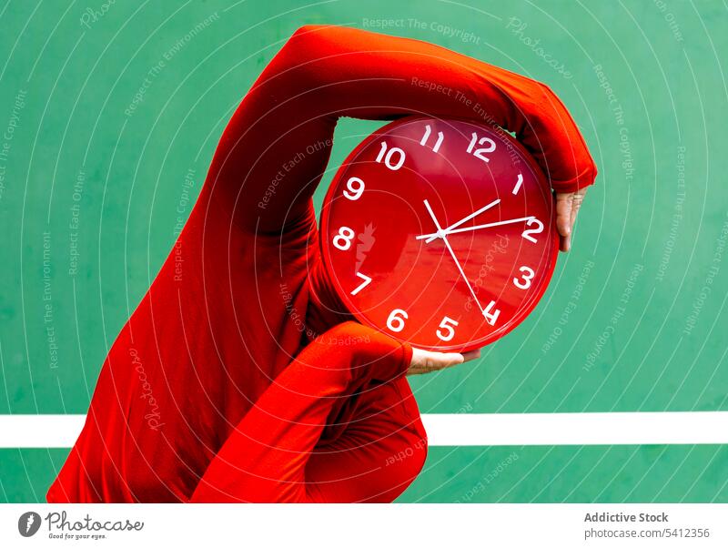 Anonymous person covering face with red clock time hide cover face hour hurry punctual concept mystery minute circle bright round deadline outfit vivid stress