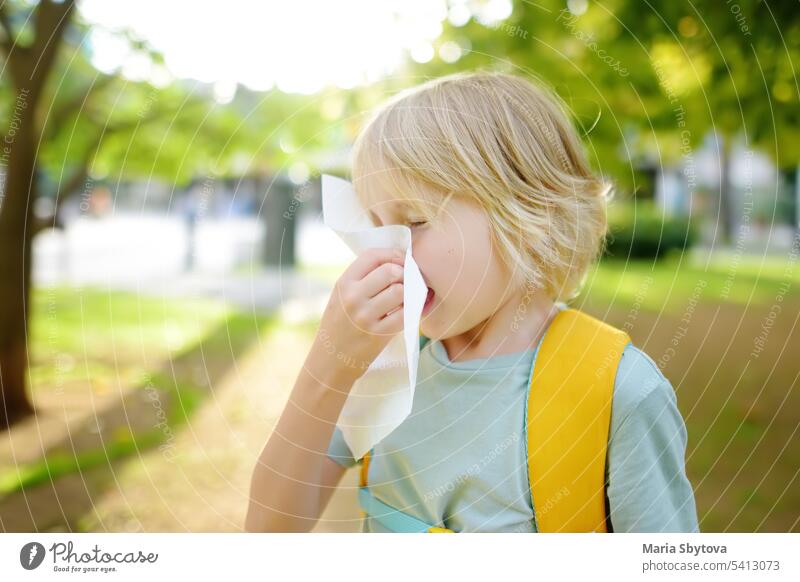 Preteen boy sneezing and wipes nose with napkin during walking in summer park. Flu season and cold rhinitis. Allergic kid. child allergic sneeze sick cough snot