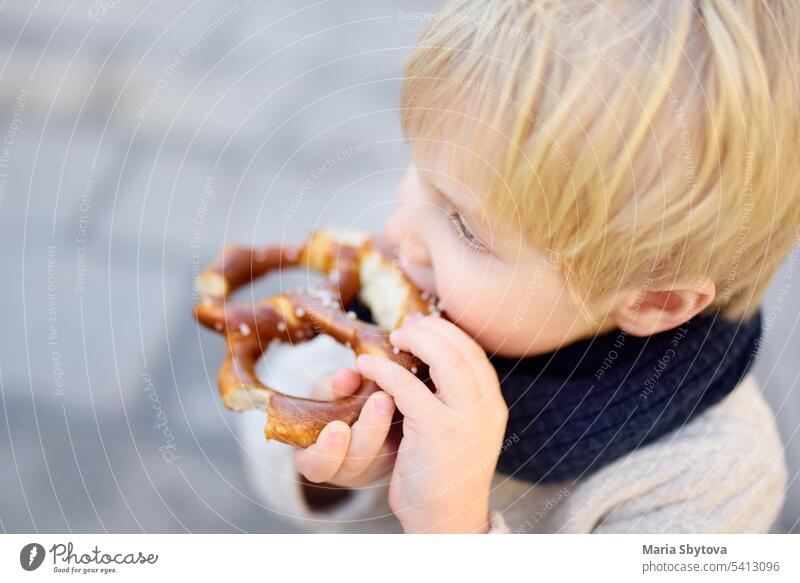 Little tourist eating traditional bavarian bread called pretzel munich kid outside child meal food travel city building happy portrait street vacation bakery