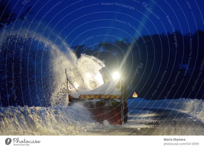 A snowplow truck clearing a snow-covered road in the European Alps while a snowstorm in the night. Drifts and snow drifts during a snowfall. winter snowblower