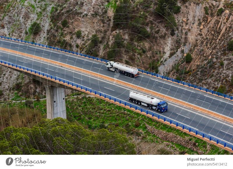 Two fuel tanker trucks crossing on a highway over a bridge, aerial view. traffic combustible gasoline transport viaduct diesel logistic distribution trailer