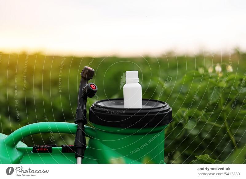 White little bottle of pesticide, herbicide for protecting plants from diseases and pests with mock up stands on container sprayer on natural green garden background. Agricultural seasonal work