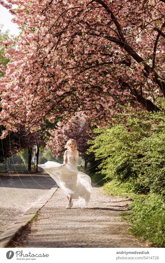 woman's day. beautiful young woman in luxury long dress near blossoming of sakura. stylish girl near blossoming sakura flowers on background in the spring park. Harmony with nature concept