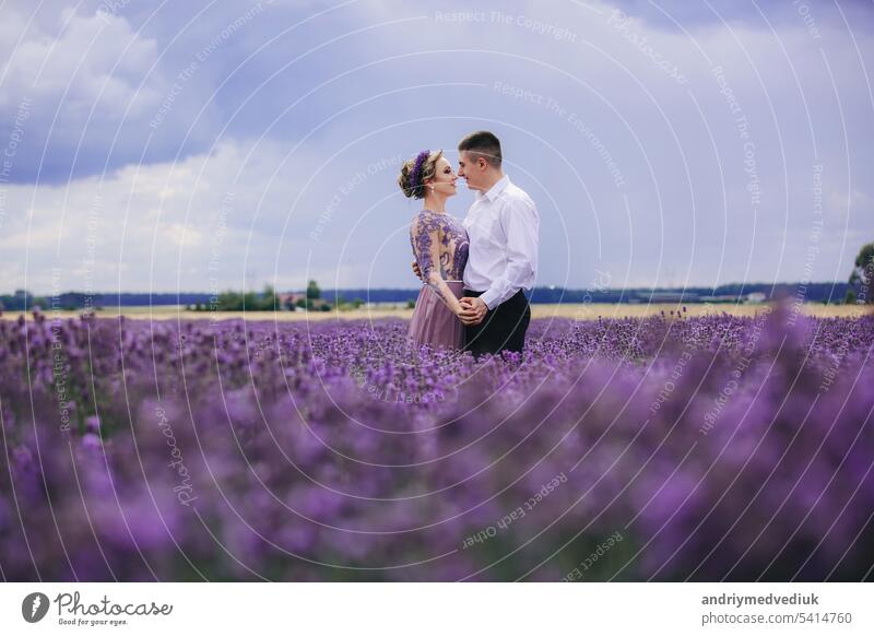 Young couple in love hugging and walking in a lavender field on summer day. girl in a luxurious purple dress and with hairstyle people together beautiful young