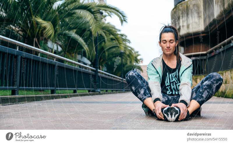 Woman runner with closed eyes relaxing sitting on the floor after training woman female resting break meditation tired town stretching holding leg arm happy