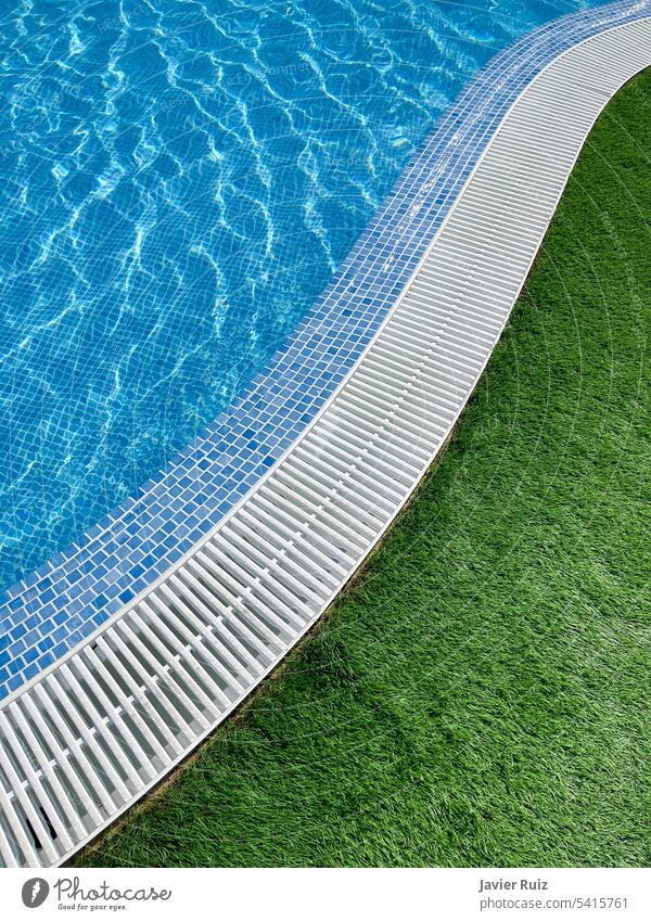 edge of an s shaped swimming pool, with crystal clear water, a white pool trellis and green grass summer blue vertical crystalline holiday lattice tiles