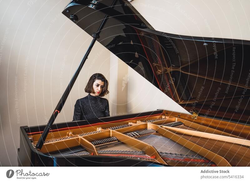 Young woman playing notes behind a piano musician young slim elegant room pianist instrument keyboard art sound performance female melody classical closed eyes