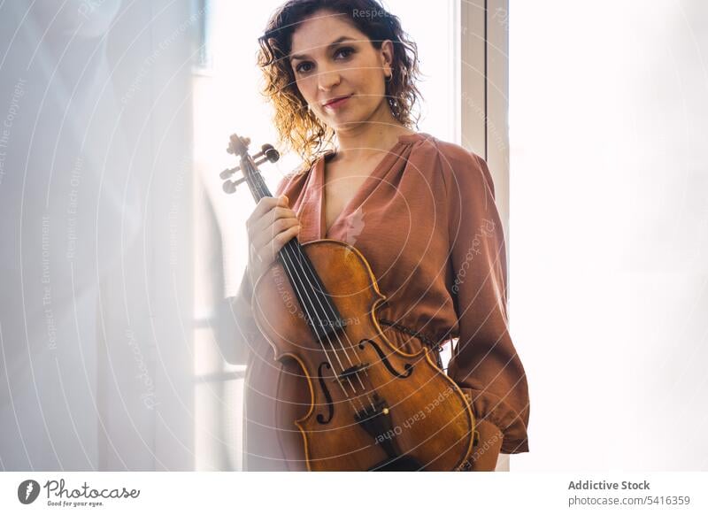 Young smiling woman with violin pregnant musician young motherhood elegant room window instrument cheerful art sound playing performance female melody violinist