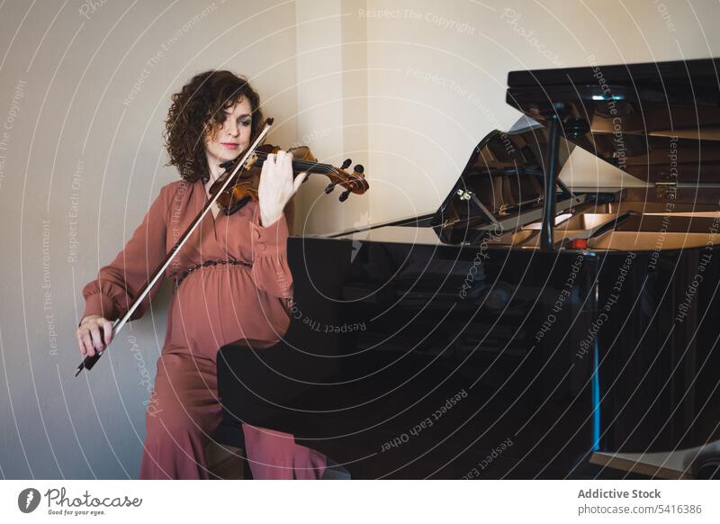 Pregnant woman playing on violin near piano in room pregnant musician attractive young curly hair beautiful closed eyes female belly sitting lifestyle relax