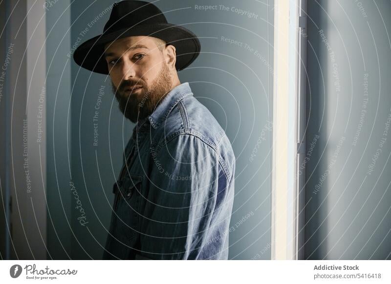 Handsome man in hat looking at camera in room handsome thoughtful bearded adult model young confident male casual stylish leisure stubble lifestyle unshaven
