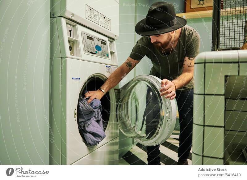 Handsome man folding laundry into washing machine handsome bearded adult model young confident male casual looking household stylish leisure stubble lifestyle