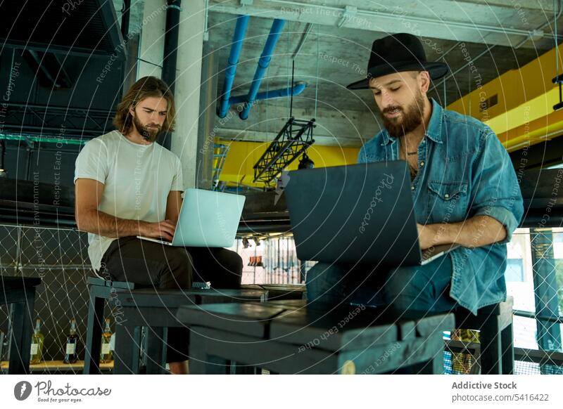 Men sitting and working on laptops indoors men handsome friendship adult cooperation lifestyle together mustache happiness bearded model young discussing