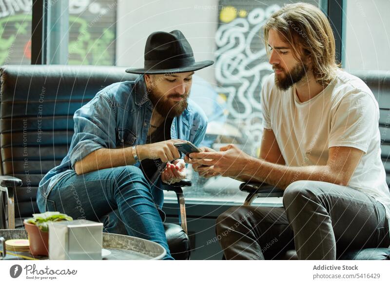 Men sitting and using phone in cafe men pointing finger smartphone friendship smiling talking enjoying adult handsome lifestyle together mustache happiness
