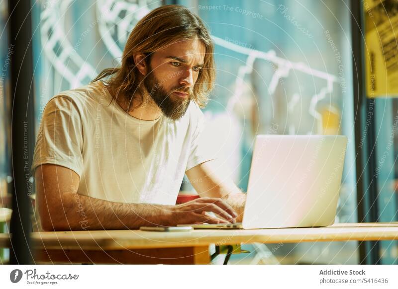 Handsome man sitting at table and typing on laptop handsome mustache working adult lifestyle stubble hairstyle happiness bearded model young confident