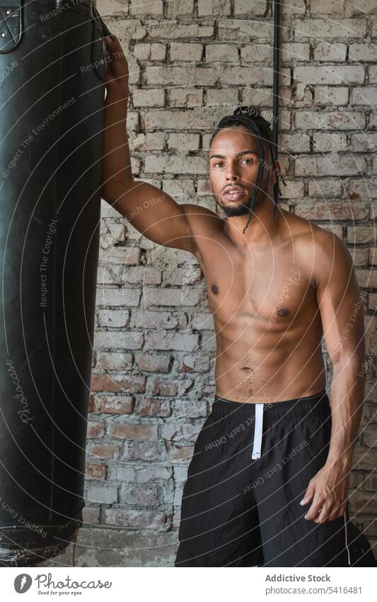 Confident black boxer in gym man boxing bag african american shirtless leaning muscular sport workout male strength power training fitness determination