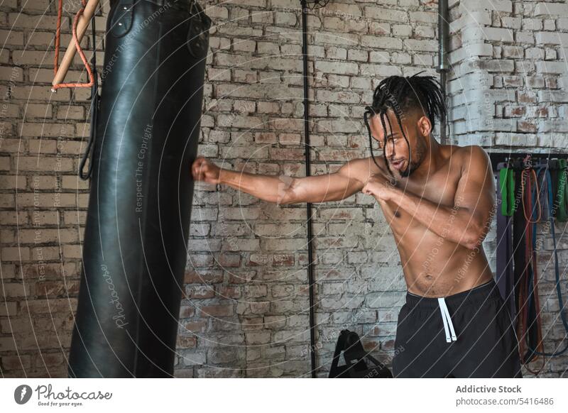 Black guy boxing in gym man bag punching workout shirtless african american sport muscular male young fitness athlete strength power fighter exercise training