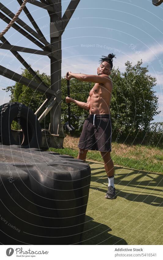 Muscular black guy hammering tire in outdoor gym man exercise hitting shirtless muscular effort workout athlete male fitness sport strong power heavy equipment