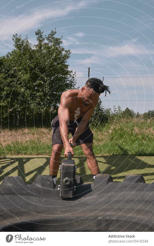 Muscular black guy hammering tire in outdoor gym man exercise hitting shirtless muscular effort workout athlete male fitness sport strong power heavy equipment