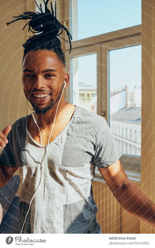 Cheerful ethnic male listening to music man hairstyle cornrows braided earphones dance thumbs up young african american person handsome positive attractive