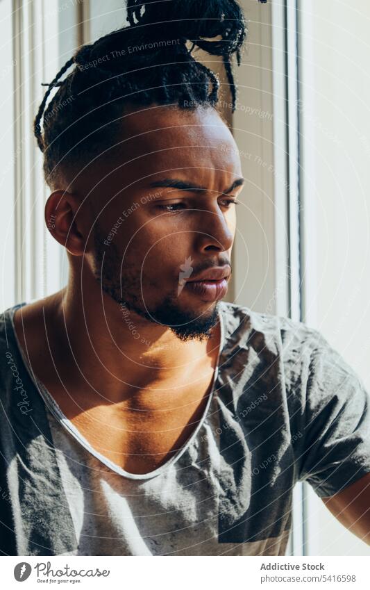 Thoughtful ethnic male sitting on windowsill man hairstyle cornrows braided young thoughtful african american black person handsome positive attractive relaxed
