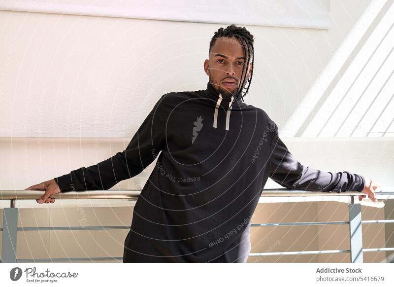 Trendy ethnic male standing indoors man braided hairstyle pigtails cornrows stylish staircase young african american person handsome attractive thoughtful