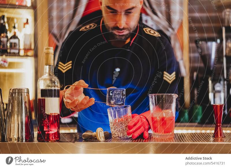 Bartender in red gloves holding big ice cube i hand bartender alcohol nightclub mixing stirring preparing barman cocktail uniform glass drink beverage alcoholic