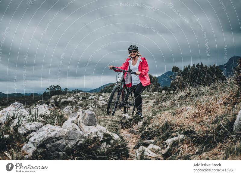 Anonymous female bicyclist on rocks woman bicycle helmet sea landscape extreme young person cheerful active sportive walking lifestyle ride bike travel