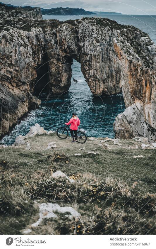 Female bicyclist on rocks woman bicycle cliff anonymous helmet sea landscape extreme female young person sportive smiling walking lifestyle ride bike travel