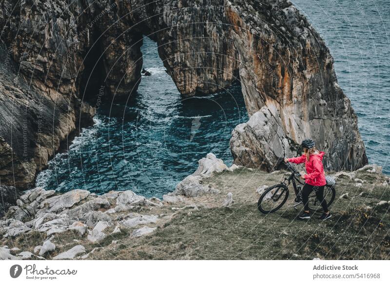 Female bicyclist on rocks woman bicycle cliff anonymous helmet sea landscape extreme female young person cheerful sportive smiling walking lifestyle ride bike