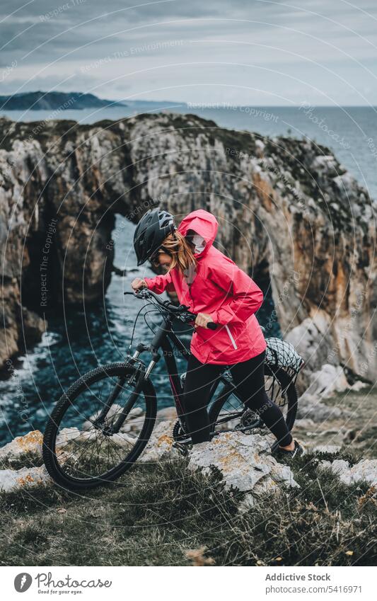 Female bicyclist on rocks woman bicycle cliff helmet sea landscape extreme female young person cheerful active sportive smiling walking lifestyle ride bike