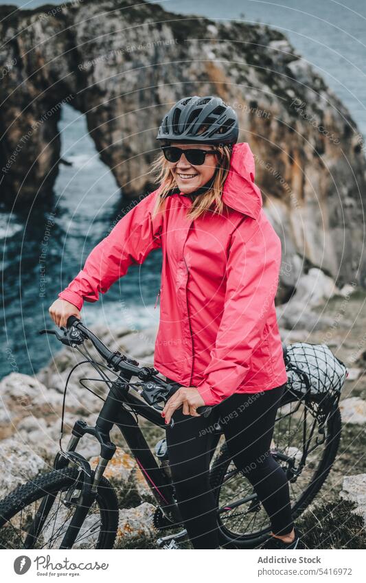 Female bicyclist on rocks woman bicycle cliff helmet sea landscape extreme female young person cheerful active sportive smiling walking lifestyle ride bike